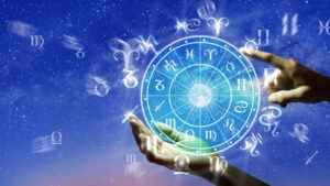 Mãos humanas apontando para um círculo com os doze signos do zodíaco, em um fundo de céu estrelado.