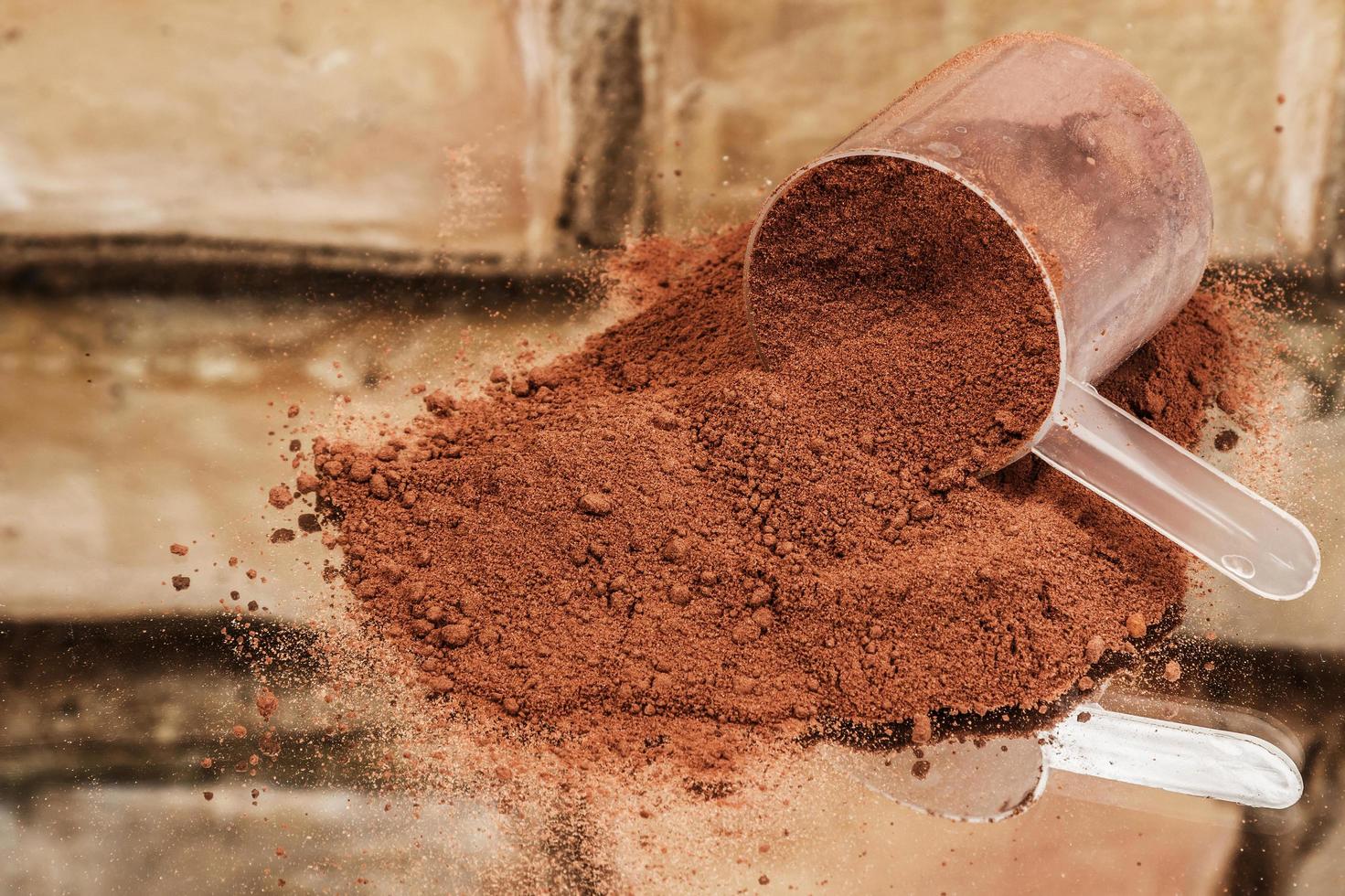 Suplemento em pó de cor achocolatada derramado com colher medidora transparente