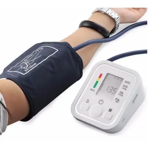 Braço de uma pessoa sendo aferido com um medidor de pressão arterial digital. O aparelho exibe os números da pressão, com leitura de 135 mmHg.