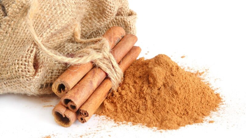 Canela em pau amarrada ao lado de canela em pó sobre fundo branco
