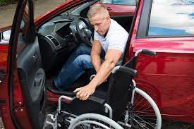 Homem com deficiência física se preparando para sair de um carro adaptado, posicionando a cadeira de rodas ao lado do veículo