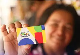 Mãos de adulto e criança segurando o cartão do Bolsa Família, simbolizando o impacto familiar do programa.